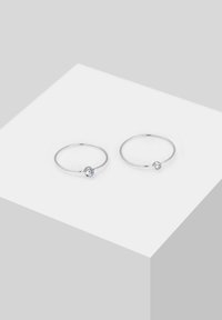 Pendientes de aro de plata con una pequeña gema transparente en el centro. Diseño circular simple con un acabado pulido.