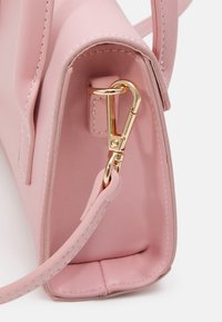 Růžová kožená kabelka s hladkou texturou, zdobená zlatým kováním a odnímatelným popruhem, představující čisté linie a jemné detaily šití.