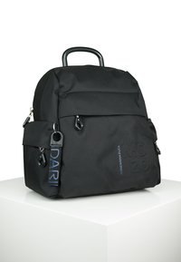 Zaino nero realizzato in tessuto testurizzato. Presenta una maniglia superiore, diverse tasche con zip e un logo in rilievo ben visibile sulla parte anteriore.