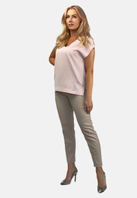 Jasnoróżowa bluzka z krótkim rękawem i dekoltem w serek, zestawiona z beżowymi dopasowanymi spodniami oraz wzorzystymi szpilkami, o gładkiej fakturze.