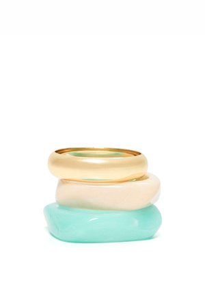 Három vastag gyűrű egymásra rakva, arany, krém és áttetsző türkiz árnyalatban, sima lekerekített formákkal és fényes felülettel.