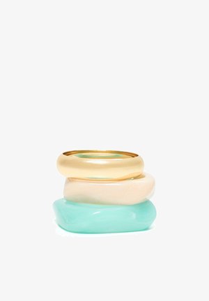 Pile de trois bagues épaisses en or, crème et turquoise translucide, avec des formes arrondies et une finition brillante.