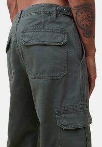 Harmaat cargo-housut, jotka ovat valmistettu kestävästä kankaasta. Niissä on kaksi takataskua ja yksi sivutasku, ja ne kiinnitetään kahdella napilla vyötäröllä.