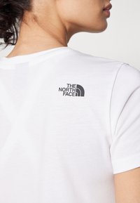 Vit bomullströja med en svart logo av The North Face på övre ryggen, korta ärmar och en klassisk rundhalsdesign.