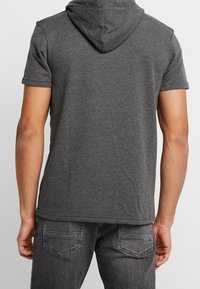 Szara bluza z krótkim rękawem wykonana z miękkiej tkaniny, o luźnym kroju i niewielkim kapturze z tyłu. Prosty design bez widocznych wzorów.