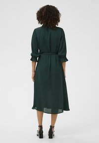 Rochie lungă, verde închis, dintr-un material ușor, având talie strânsă, mâneci de trei sferturi și un tiv ușor evazat.