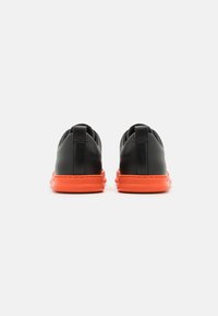 Chaussures en cuir noir avec une semelle en caoutchouc orange, affichant un design minimaliste et une languette arrière pour un enfilage facile.