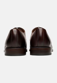 Braune Leder-Dressschuhe mit glatter Oberfläche, abgerundetem Absatz und kontrastierenden Nähten, einem eleganten Design und minimalistischen Akzenten.