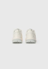 Une paire de baskets blanches vue de derrière, avec des accents gris et des languettes sur un fond clair.