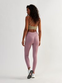 Athletic outfit featuring a tan cropped top with crossover straps and soft pink high-waisted leggings with a smooth finish, paired with white shoes.