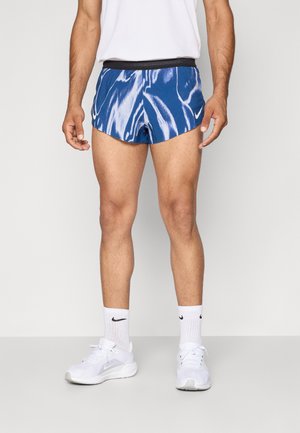 Shorts de sport à motif bleu avec une taille noire, portés avec des chaussettes blanches et des baskets. Présente un design ondulé et une coupe ajustée.