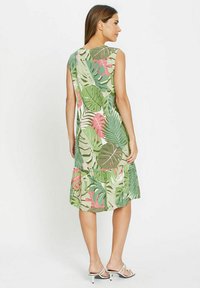 Ärmelloses, knielanges Kleid mit einem grünen und pinken tropischen Blättermuster, das einen gestuften Saum und ein leichtes Material aufweist.