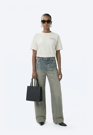 Žena s krátkymi vlasmi, ktorá nosí slnečné okuliare, biele tričko Diesel, široké vyblednuté džínsy, čierne špicaté topánky a drží čiernu kabelku Ted Baker.