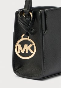 Schwarze Lederhandtasche mit strukturierter Oberfläche, versehen mit einer goldfarbenen, runden MK-Logo-Plakette und einem eleganten Design mit kurzem Henkel.
