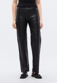 Μαύρο δερμάτινο παντελόνι με εφα ρμοστή μέση και φαρδιά γραμμή. Διαθέτει ορατές ραφές και λεία υφή, τονισμένη από μια κομψή φινιρίσμα.