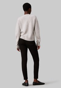 Suéter texturizado gris claro con dobladillos y puños de canalé, combinado con pantalones negros ajustados y zapatos planos negros, visto desde la parte trasera.