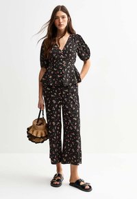 Blouse peplum à imprimé floral noir avec manches bouffantes, détails de boutons, associée à un pantalon court assorti à imprimé floral et des sandales à glisser noires.