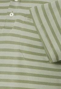 Polo w paski w jasnym zielonym i białym kolorze z zapięciem na guziki, krótkimi rękawami i małą kieszonką na piersi. Teksturowana tkanina z widocznym przeszyciem.