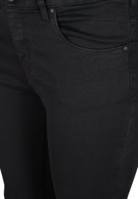 Black denim jeans feature a fitted design, five-pocket styling, and a smooth texture with subtle stitching details.