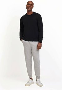 Schwarzer Strickpullover, graue Jogginghose und weiße Turnschuhe. Das Outfit zeichnet sich durch eine legere Passform mit einfachem Design und weicher Textur aus.