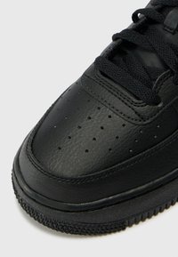 Sapatilhas de couro preto com textura suave, bico redondo, detalhes perfurados e atacadores pretos. Apresenta uma sola exterior de borracha texturizada.