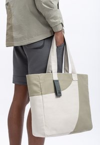 Canvas totebag met lichtgroene, beige en witte panelen. Heeft stevige handvatten en een label aan de voorkant met een schaarontwerp.
