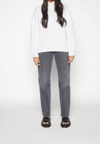 Felpa bianca oversize, jeans dritti grigio scuro e sandali neri a scivolo. Tessuto morbido, vestibilità casual e design semplice.