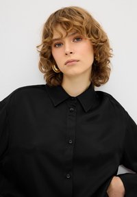 Camicia nera con bottoni, colletto e vestibilità ampia. Tessuto testurizzato, sei bottoni sul davanti e maniche leggermente arrotolate.