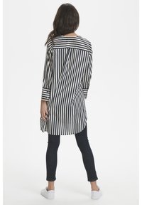 Túnica a rayas en azul marino y blanco, con corte recto, mangas largas y dobladillo curvado. Combinada con jeans oscuros y zapatillas blancas.