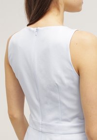 Svetle modré šaty s hladkou texturou, přiléhavým střihem a skrytým zipem na zadní straně. Obsahují švové detaily a bezramenný střih.