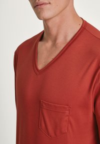 Rode v-hals t-shirt van zachte stof, met een borstzak en gestructureerde stiksels langs de halslijn voor extra detail.