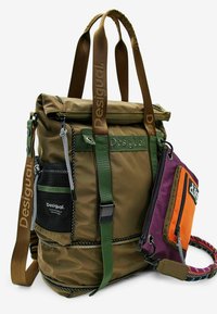 Olivengrøn nylon rygsæk med flere lommer, justerbare stropper og meshdetaljer på siden. Har en aftagelig lilla og orange pung.