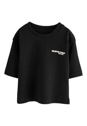 T-shirt nera in cotone a maniche corte, vestibilità oversize, colletto girocollo a coste. Presenta un testo bianco: "DIVERTIMENTO ILLIMITATO DAL 1982" sul petto.