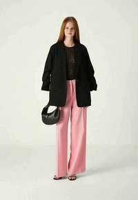 Blaser noir surdimensionné, haut noir transparent, pantalon large rose clair, et un petit sac à main noir. Des sandales plates complètent le look.