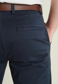 Mornarine hlače od glatkog materijala slim fit kroja, s jednim zadnjim džepom i smešnim kožnim remenom.