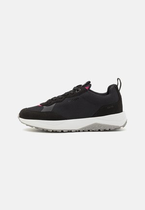 Black athletic shoe with mesh and suede materials, rounded toe, white midsole, and a textured gray outsole. Contains pink accents on the side.
