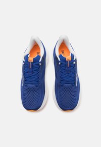 Des chaussures de sport bleues avec une tige en maille respirante, des semelles blanches et des accents orange sur la languette et les semelles intérieures. Les lacets sont bleus.