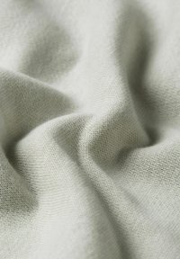 Tissu doux de couleur gris clair avec un tissage texturé présenté dans une disposition drapée, mettant en valeur sa surface lisse et ses plis délicats.