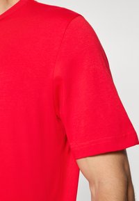 Červené tričko s krátkým rukávem vyrobené z měkké bavlněné látky. Má klasický kulatý výstřih a čisté švy na rukávech a spodním lemu.