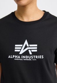 T-shirt en coton noir arborant un logo blanc avec une étoile abstraite et des rayures, accompagné du texte "ALPHA INDUSTRIES, KNOXVILLE, TENNESSEE, É.-U."