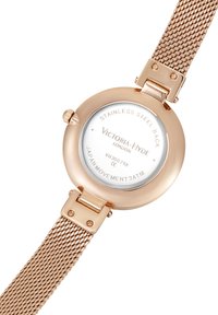 Orologio in acciaio inox oro rosa con cinturino a rete, cassa rotonda e quadrante bianco. Caratterizzato da un fondello in vetro con dettagli incisi.