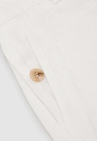 Close-up of white linen fabric with beige marbled button and stitched seam details.