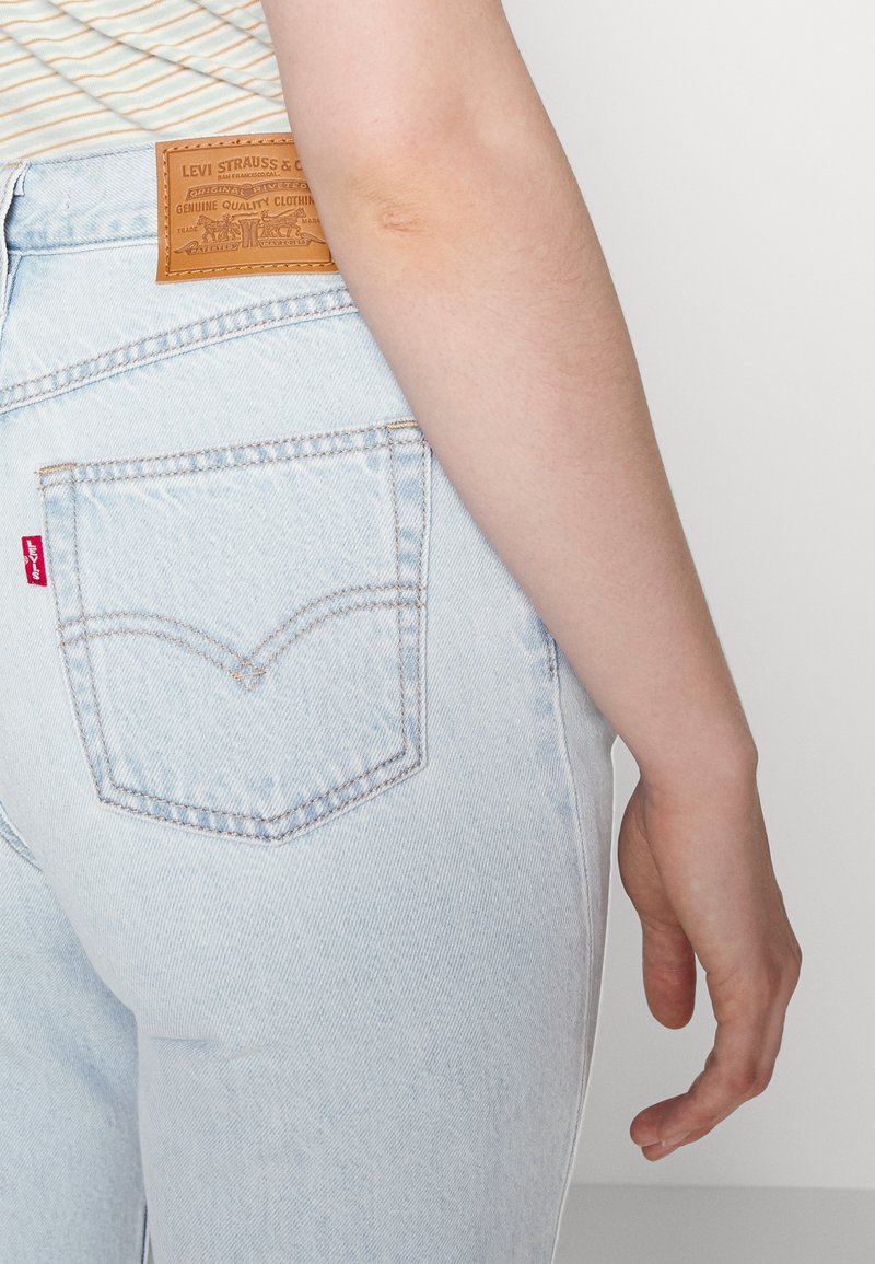 Helle blaue Jeans mit einer Gesäßtasche, versehen mit einem roten Logoetikett und einem braunen Lederetikett mit Branding am Bund.