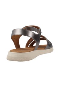 Sandalias metálicas plateadas con tiras y suela blanca de perfil bajo, con plantilla acolchada marrón y detalle de correa ajustable en el tobillo.