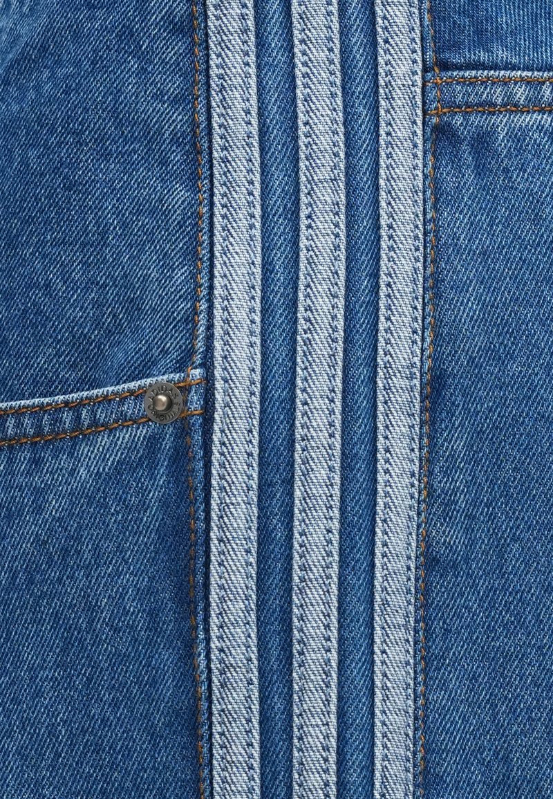 Gros plan sur un tissu en denim bleu avec des rayures verticales plus claires, une couture orange et une partie d'une poche avec un rivet métallique.