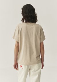 T-shirt beige à manches courtes avec une coupe décontractée, fabriqué en tissu doux ; présente un design simple et un ourlet légèrement incurvé.