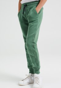 Gröna sweatpants med dragsko i midjan, sidofickor och tryckt text längs benet. Matchade med vita sneakers. Slätt bomullsmaterial.