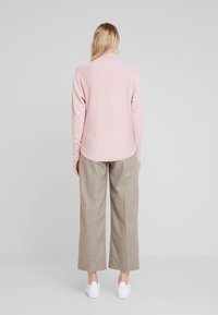 Maglietta a maniche lunghe di un delicato rosa, con orlo arrotondato, abbinata a pantaloni beige a gamba larga e sneakers bianche. Dettagli di tessuto strutturato visibili.