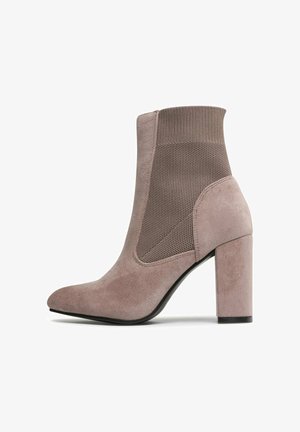 Fioletowy zamszowy botek za kostkę z dzianinową boczną wstawką i blokowym obcasem, z charakterystycznym spiczastym noskiem i gładką podeszwą.