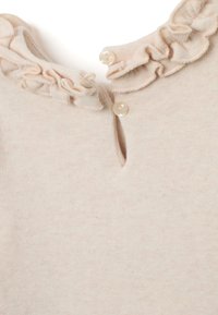 Hellbeige Oberteil mit rundem Ausschnitt, verziert mit einem Rüschensaum und einer kleinen Schlüsselöffnung, akzentuiert durch zwei runde Knöpfe. Weiche Textur.